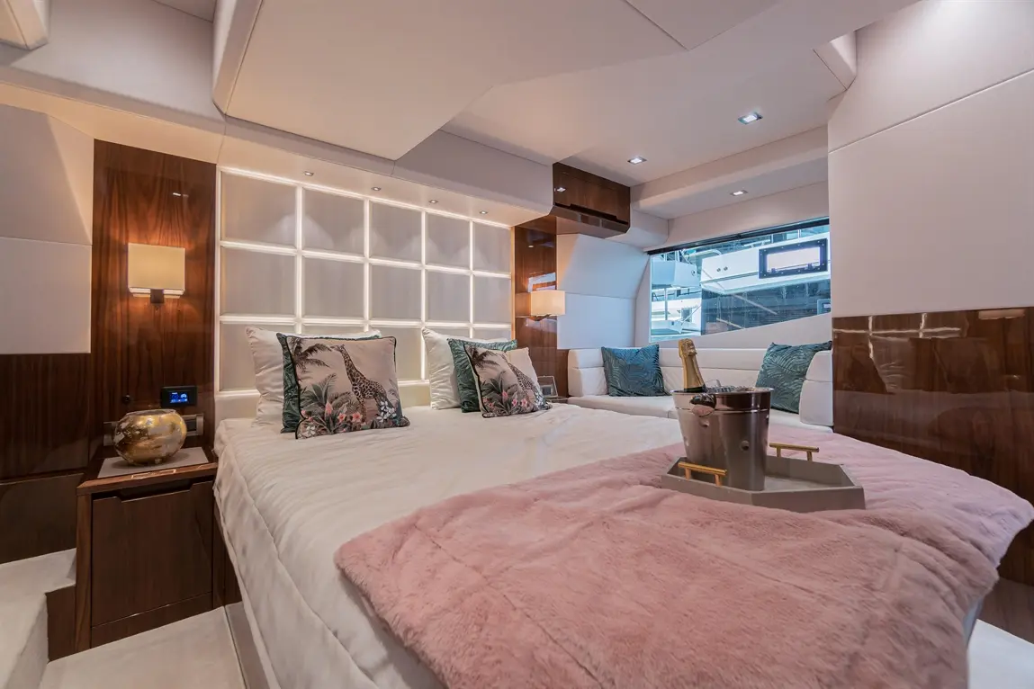 Luxurious yacht interior featuring a double bed, plush pillows, a pink throw, and a window with a view of the marina.